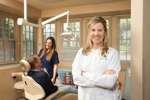 Dr. Jacqueline Bennett stands in a dental exam room with a dental patient and hygienist in the background